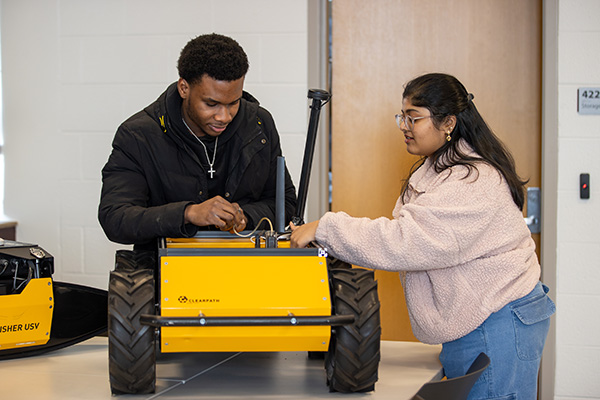 two students connecting wires inside a robotic yellow vehicle