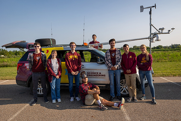 a group of people posing for a photo in front of a central michigan university branded weather chasing vehicle