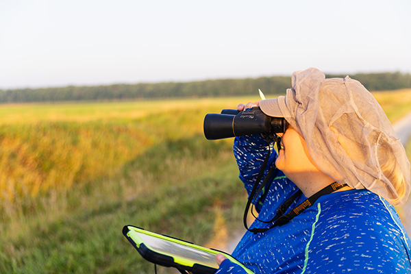 a person holding a tablet and looking through binoculars in a large field