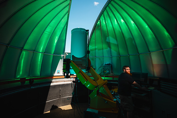 a man in a partially open green dome with a large telescope