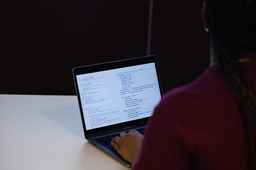 A student in front of a laptop with a screen full of data.