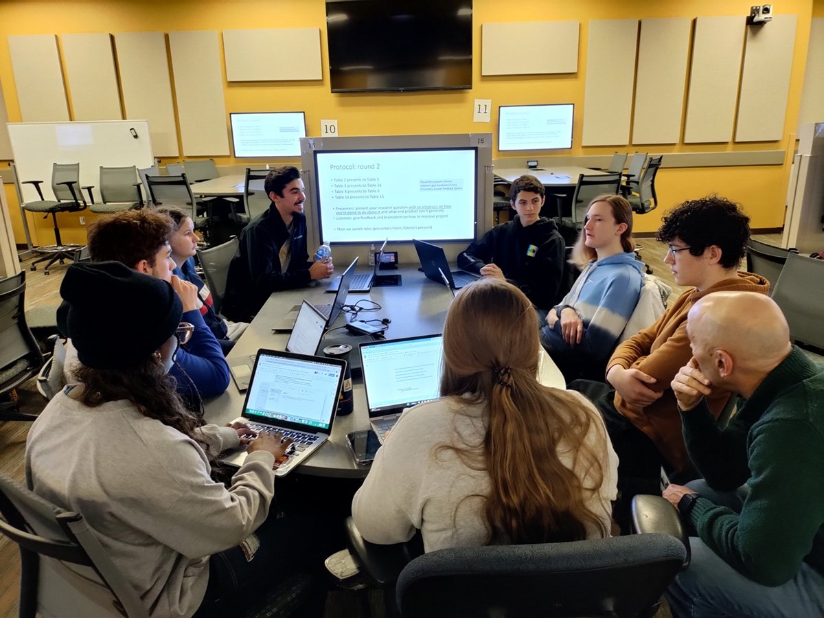 A group of InSciTE students sit around a desk in one of our active learning classrooms having a discussion as a faculty member monitors.