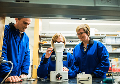 Jennifer Schisa and two students examining a sample under a microscope.