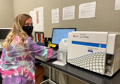 A student in a tie-dye lab coat uses the flow cytometry equipment.