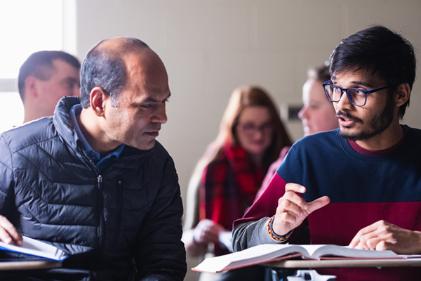 Two graduate students having a discussion in the classroom.