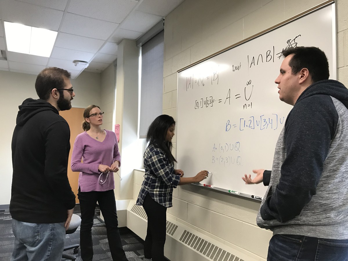 Mathematics students discussing formula on whiteboard.