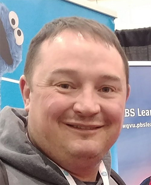 A man with short hair standing in front of a banner with cookie monster on it.