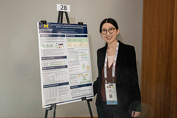 Linxi Zheng in a suit coat standing in front of a research poster.