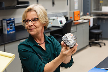 A woman in a lab holding a geologic sample in her hand.