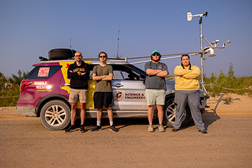 A group of people standing next to a vehicle with weather measuring gear attached to it