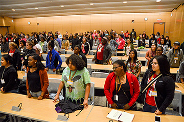 A large group of students standing behind tables in a large room.