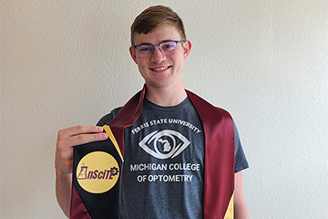 A student in a t-shirt in front of a neutral background holding a graduation sash with the InSciTE logo on it.