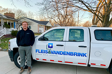 Mike Visscher in grey pants and a blue shirt standing in front of a white pickup truck with the company name of Fleis and Vandenbrink on the side.
