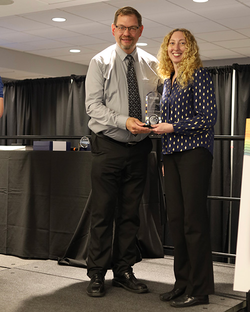 20250619_VanBruggenAward A man and a woman standing on a stage holding an award between them.