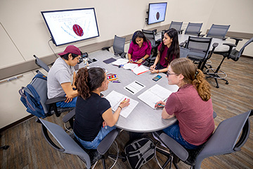 a group of students sitting around a table with notebooks open in front of them