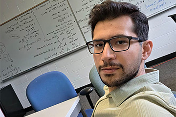 a man in glasses taking a selfie in front of a white board full of mathematical equations