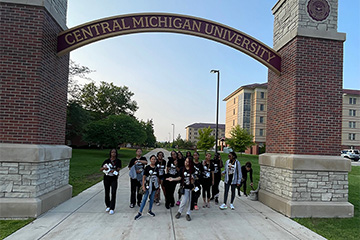 A group of students standing in between to large brick pillars and underneath an arch that says Central Michigan University.