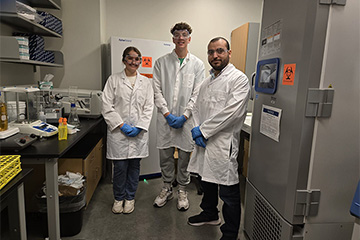 three people wearing white lab coats and blue gloves standing in a lab
