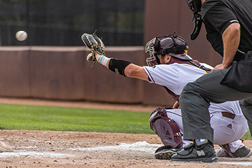 Catcher for the CMU Baseball Team about to catch a ball that has been pitched with an umpire standing behind him.