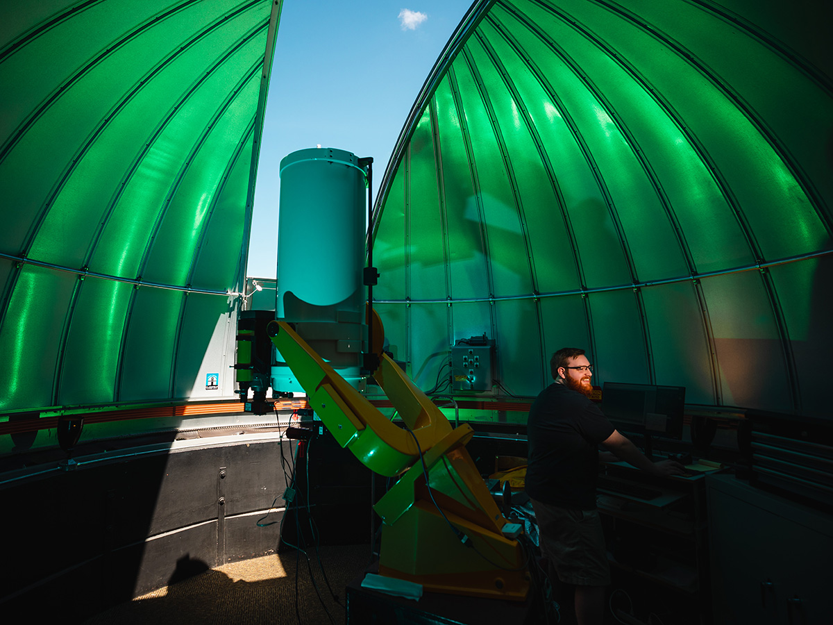 a man in a green dome typing on a computer next to a large telescope