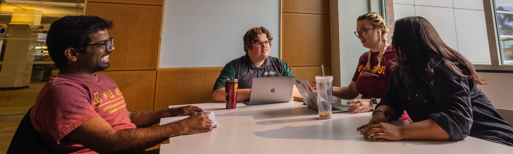 Students collaborate at a study table inside Park Library at Central Michigan University, with natural light from large windows and the library’s curved glass exterior visible outside.