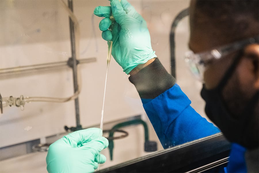 A student researcher wearing gloves, a lab coat and safety glasses works with a pipette.