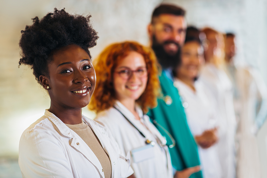 A group of health professionals in white coats stand shoulder to shoulder smiling at camera