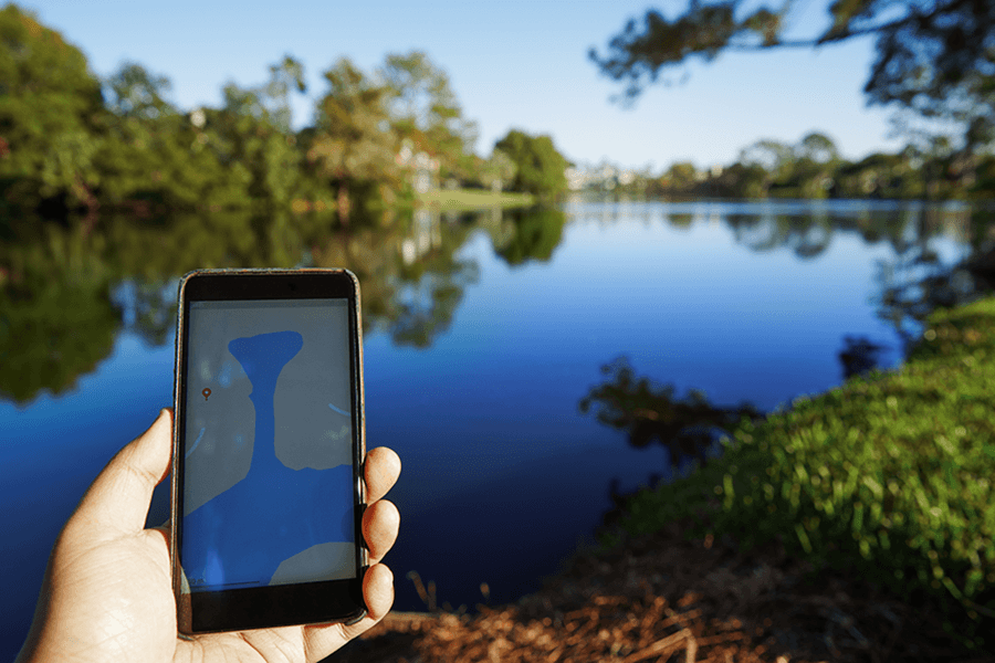 A hand holds a phone in front of a lake.