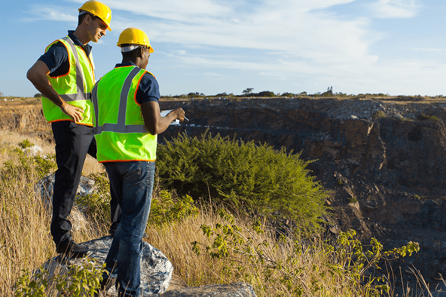 Two people in hard hats and vests look out over a quarry.