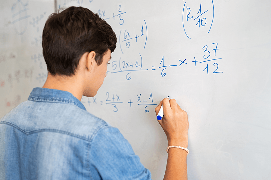 A student solves a math problem on a white board.