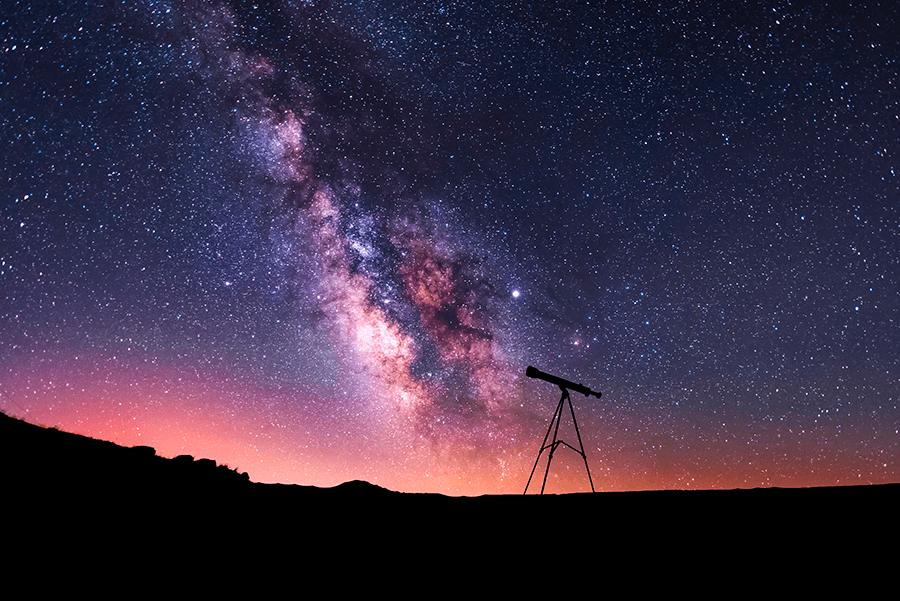 A telescope in front of a starry night sky.