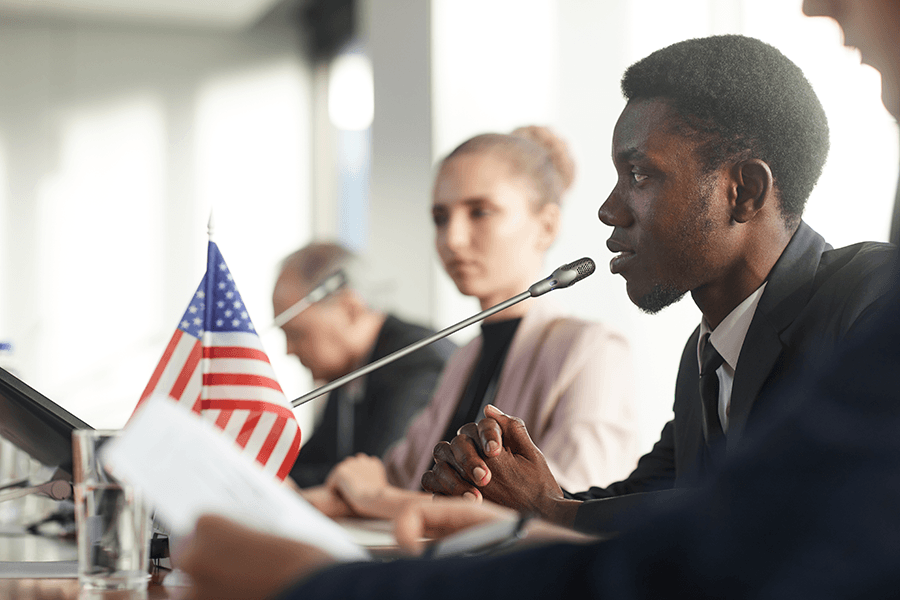 A student speaking on a conference with the US flag on his table.