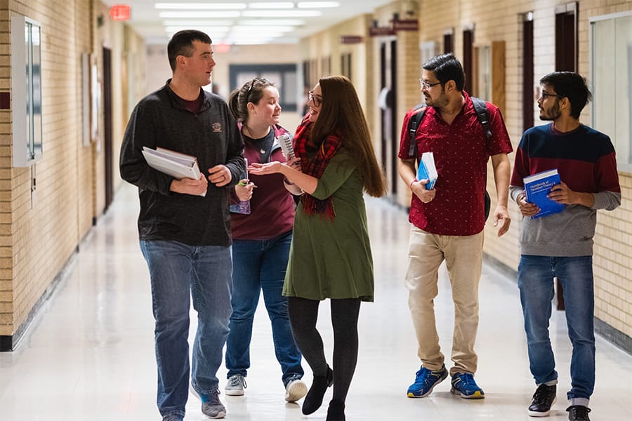 A group of mathematic students walk down the hallway on campus.