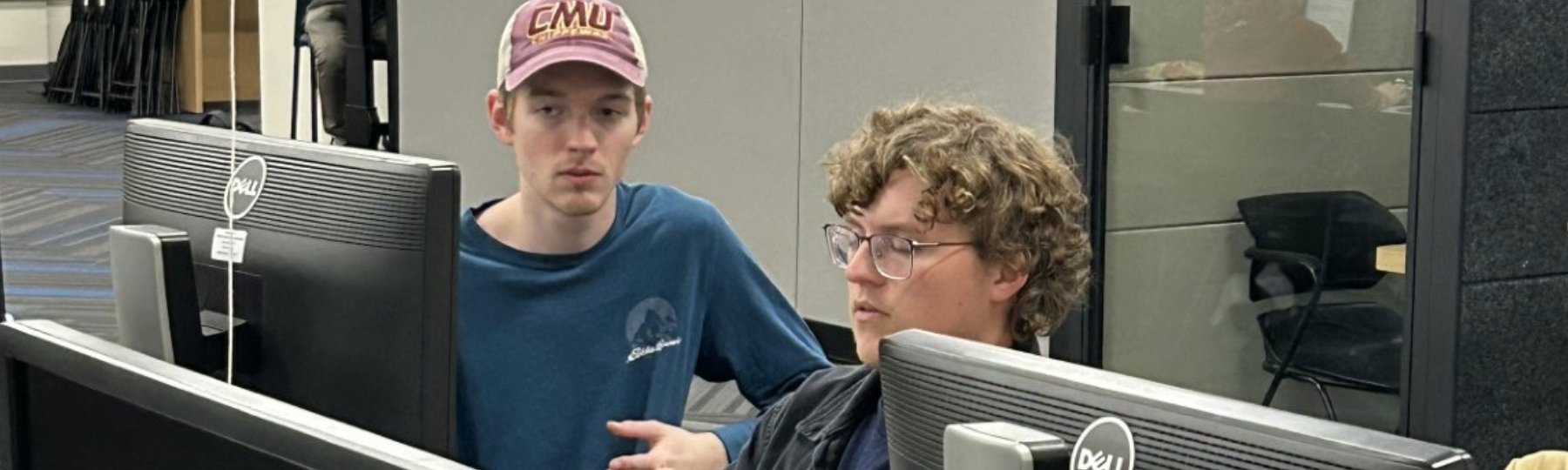 Three cybersecurity students sit at monitors in a computer lab.