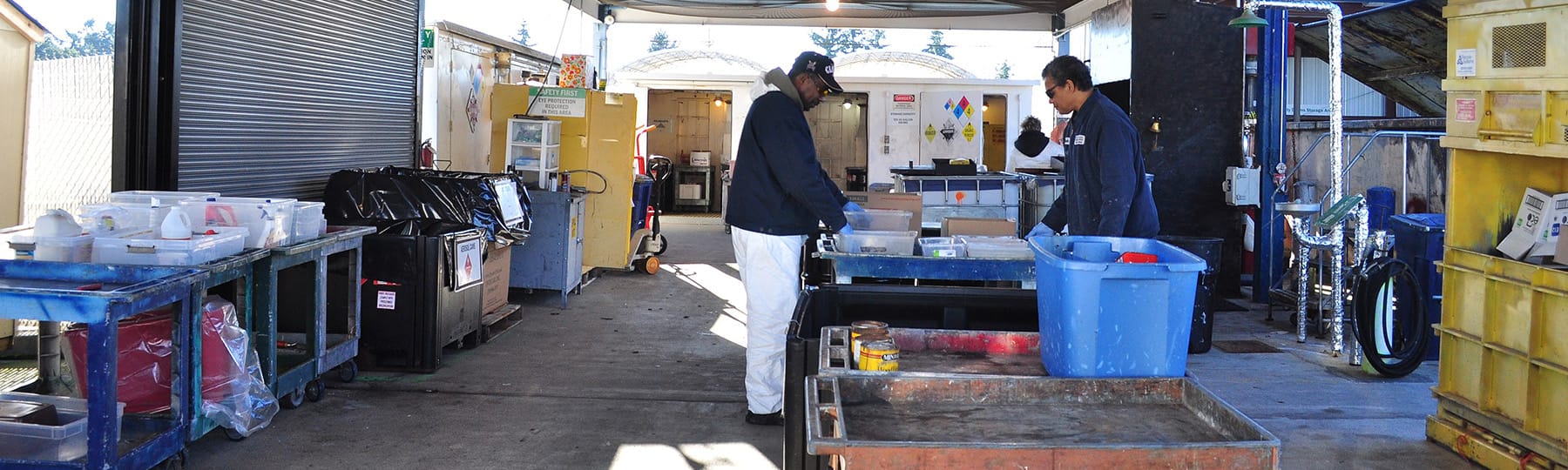 Two men stand at a household hazardous waste collection facility sorting materials.