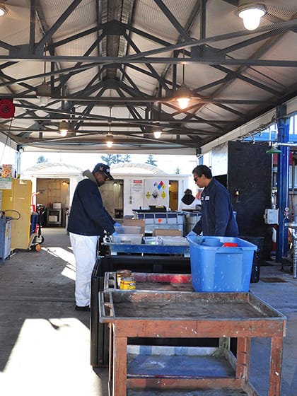 Two men stand at a household hazardous waste collection facility sorting materials.