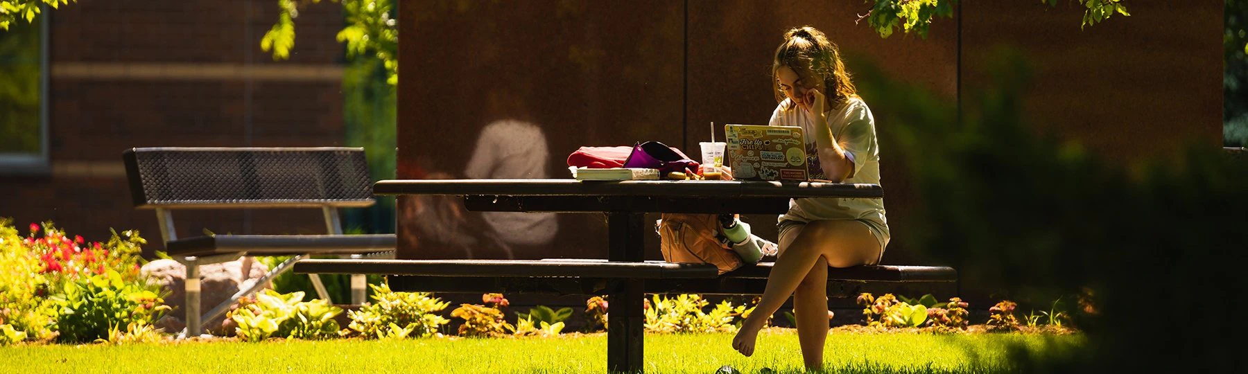 A female student working on a computer while sitting on a table outside.