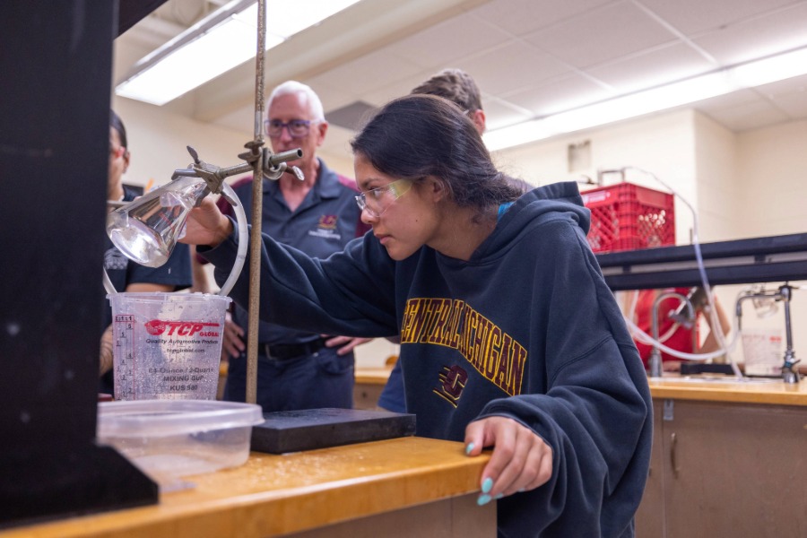 female student crouches down to read measurements off a beaker in a geology hydraulics lab
