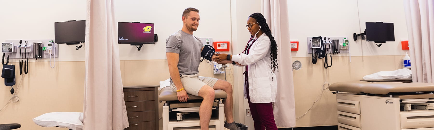 A pre-physician assistant student uses a blood pressure cuff and stethoscope to take a the blood pressure of a male patient.