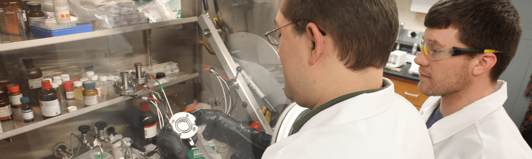 Two students wearing lab coats examine materials in a research lab.