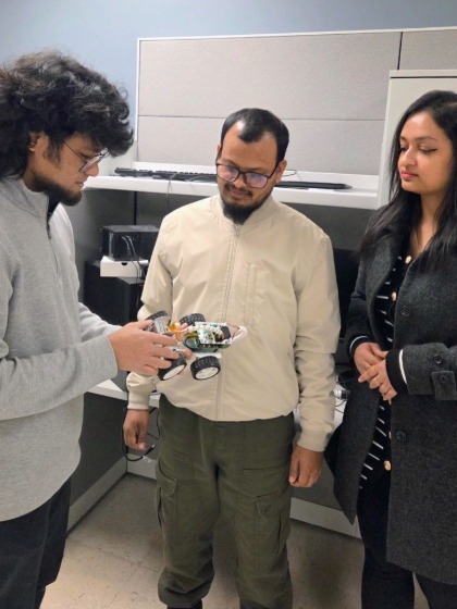 two engineering students and a professor gather around a small robot car
