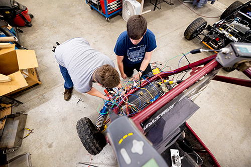 Two students attaching components to the front end of the competition baja car.