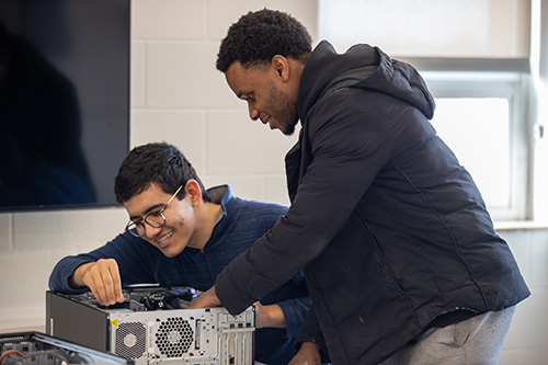 Two students replacing parts inside a computer.
