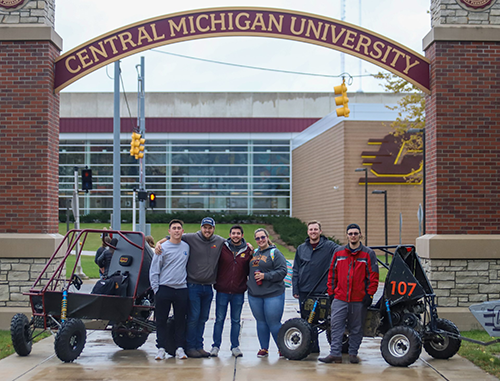 A group of students standing with 2 CMU Baja cars in front of the CMU Arch.