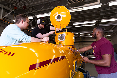 A group of students measuring a part of a small yellow submarine.