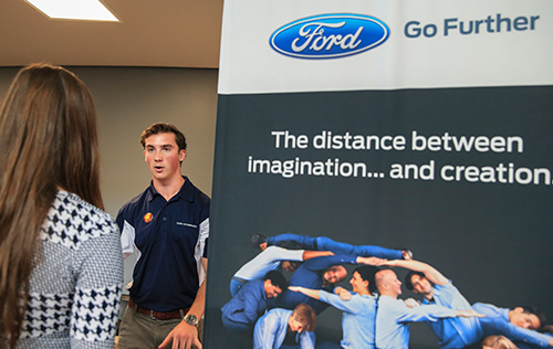A man and woman standing next to a Ford banner.