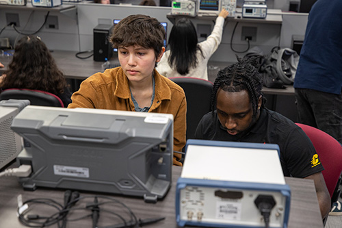 A group of people working on electronic equipment in an electronics lab.