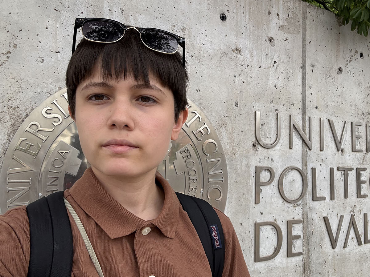 A student in a brown shirt and sunglasses looking at the camera