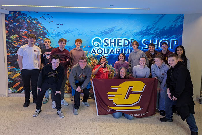 A group of students holding a Central Michigan University flag standing in front of the Shedd Aquarium Shop.