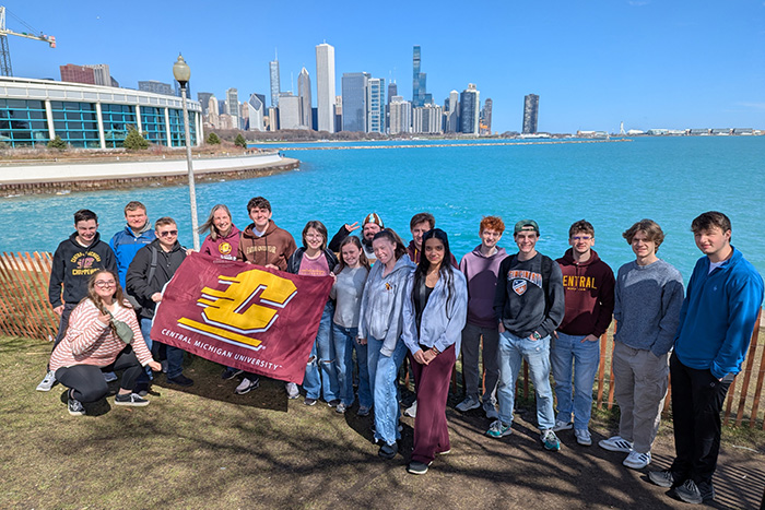 A group of students holding a Central Michigan University flag with Chicago in the background behind them.